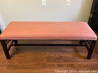 Front view of a rectangular wooden bench with pink upholstered seat and decorative nailhead trim.