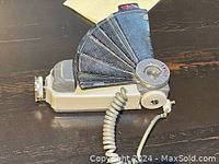 Side angled view of the vintage Anglo Depth of Field camera accessory showing the fan-shaped adjustable aperture and coiled cable.