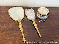 Photo of vintage vanity set items on wooden surface: hand mirror, brush, and glass holder.
