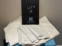 Group photo of two white tablecloths and a stack of ten matching white damask napkins laid out on a surface, showing damask floral and ornamental pattern details.