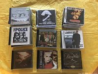 Top view of several music CDs including Highway 61 Revisited by Bob Dylan, The Fame Monster by Lady Gaga, The Essential by Blue Öyster Cult, Greatest Hits by The Police, Sgt. Pepper's Lonely Hearts Club Band by The Beatles, Jay-Z The Blueprint 2, Eurythmics Greatest Hits, Barry White All-Time Greatest Hits.