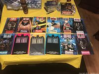Top-down photo of all 12 Batman comics laid out on a yellow surface showing the colorful cover art and titles of the comics.