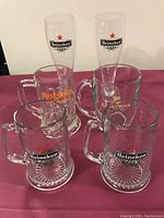 Six beer glasses and mugs on a table, 4 Heineken glass mugs, 1 Guinness mug, 1 Holsten mug