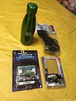 Lot items on yellow surface including Muscle Machines '58 Impala die-cast car, water bottle, power cord, and Zamboni toy in packaging