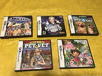 Five Nintendo DS game cases displayed on a yellow surface showing front cover art and titles.