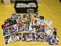 Photo showing a bin filled with a large collection of hockey and baseball cards spread out and stacked in front of the bin. Cards show various hockey players in team jerseys.