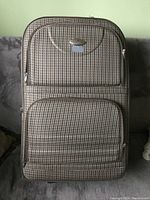Front view of suitcase shows beige and brown houndstooth fabric with two zippered front pockets and silver zipper pulls.