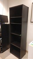 Front view of tall, dark brown manufactured wood bookcase with five shelves in a room corner.