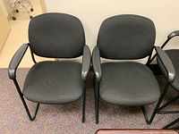 Pair of black office chairs with upholstered seats and backs, with metal sled bases and armrests, positioned side by side.
