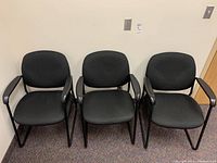 Three matching black office chairs with upholstered seats and backs, set against a cream wall, showing full front view.