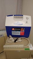 Blue and white Igloo Playmate cooler with label showing 30 can (15 L) capacity and white power cord laid on top.