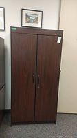 Tall manufactured wood cabinet with dark wood finish, two doors, and metal handles.