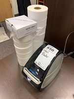 Photo showing the Dymo label maker powered on with several rolls of spare white labels beside it.