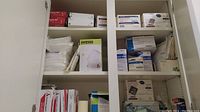 Medical supplies stored on white shelves enumerating various boxes of masks, bandages, gloves, and related items visible on multiple shelves.