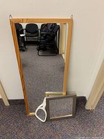 Three mirrors leaning against wall: large rectangular wood framed mirror, square wood framed mirror, and white handheld mirror.