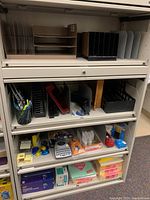 Photo of filing cabinet shelves showing various file organizers in beige, black, and brown colors alongside pen holders and other desk organizers.