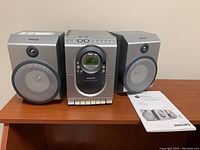 Front view of Philips MC138 stereo system with two speakers and manual on wood surface.