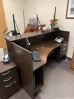 Receptionist desk with keyboard, mouse, and office phone on surface, visible locking drawers on the side, dark brown laminated finish.