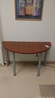 Front view of demilune table showing warm brown faux wood top and silver metal legs.