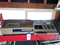 Sanyo Betacord 4000 Betamax VCR on left and Aiwa AD 1250 stereo cassette deck on right, shown powered on and side by side on shelf.