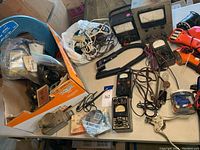 Overview of all electrical tools and meters on table including multiple analog meters, wires, rotary lineman tester, snake light, and fish tape.