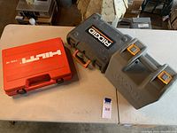 Two hard cases on a table: red Hilti case and gray Ridgid case with Ryobi molded case on the side.