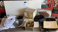 Wide view of kitchenware items including mix & serve bowls with stainless rims, cast aluminum cake pans in various shapes, candle holders, and boxed items.