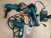 Full lot overview showing the electric drill, disc grinder, cordless circular saw, battery, and charger all arranged on a surface.