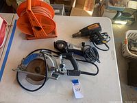 Top view of all items on a white table showing the orange extension cord on reel, SkilSaw worm drive saw, Dremel angle grinder, and Wagner heat stripper.