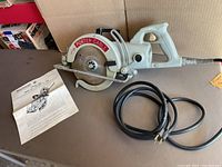 Photo showing the Rockwell Porter-Cable portable circular saw with blade guard and power cord, laid on a table with an instruction manual beside it.