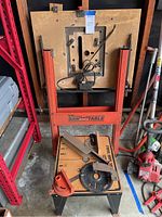 Full view of the IRS portable saw table, showing the orange frame, adjustable parts, wooden table surface, and power cord.