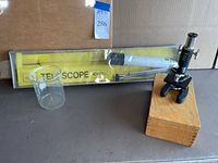 AMC 40x40mm Telescope in original yellow packaging with tripod, and Towa microscope mounted on wooden box, alongside clear glass beaker.