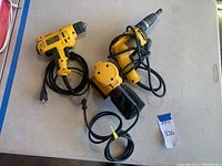 Photo showing all three power tools on a white surface including a drill, drywall screwdriver, and palm sander with power cords.