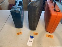 Three hard plastic carrying cases for the tools on table with labels Hammer Drill, Finish Nailer, Handheld Saw/Sander