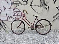 Side profile shot of a 1950s CCM single speed bicycle with maroon frame and step-through design against a graffiti wall
