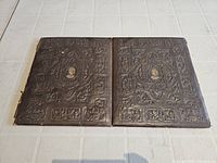 Closed view of the antique fold out photo frame showing the embossed and decorated dark brown covers with central medallions.