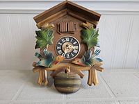 Front view of carved wooden cuckoo clock featuring bird decorations and clock face with Roman numerals.