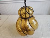 Top and side view of blown glass amber ceiling light showing bulbous segmented glass shade and metal frame with chain.
