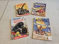 Four vintage magazines laid flat, showing front covers and condition including wear and discoloration.