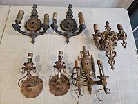 All six antique light fixtures arranged on a white table showing pairs and singles, some with missing components and wiring visible