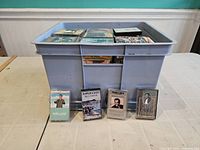 Large plastic bin filled with approximately 190 audio cassette tapes arranged inside. Four cassette cases displayed in front showing some artists titled Mario Lanza, Hawaii Calls, a portrait of a man, and Ray Price.