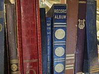 Spine view of multiple vintage record albums and binders in varying colors and designs used for storing 78 RPM records.