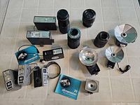 Overview of all camera lenses and multiple external camera flashes including round reflector types and Dimension 40 flashes on white tile surface.