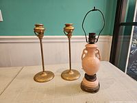 Full view of the lot showing two brass lamp bodies and one pink ceramic lamp with socket and cord