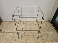 Square midcentury modern table with clear glass top and hairpin metal legs, showing rust spots.