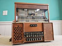 Front view showing jukebox with letter and number buttons, speaker grills, and volume level switch