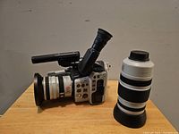Camcorder body with attached macro adapter lens and separate zoom lens on table
