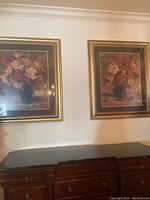 Pair of framed floral prints hanging above a piece of furniture, showing their overall appearance and gold frames.