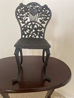 Front view of black cast iron decorative plant stand with floral and heart cutout design on backrest and detailed legs.