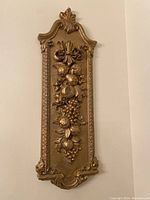 Front view showing detailed fruit and floral relief on gold painted plaster wall hanging with ornate border edges.